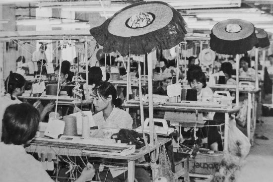 1982年，东莞，在珠三角的服装厂，客家女特有的裙式遮阳帽子挂在工作台上方。