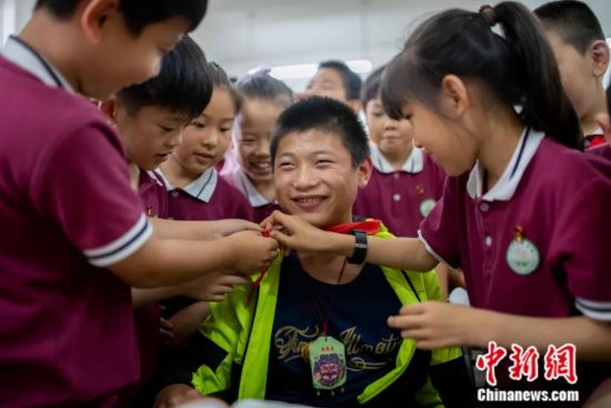 2021年6月，山西太原，患有先天性脑瘫的谷子谦第一次走进校园，同学们为他戴上红领巾。今年15岁的谷子谦是农家妇女孔爱英从小收养的多名孤残儿童之一。由于他生活不能自理，迄今还未上学，“上一天学”成了他的梦想。当日，在爱心志愿者的帮助下，谷子谦第一次走进校园，与同学们共同上课，圆了自己的“上学梦”。中新社记者 韦亮 摄