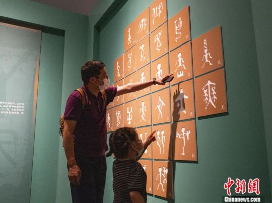 家长带着孩子在中国国家博物馆参观中国古代象形文字——金文。中新社记者 侯宇 摄