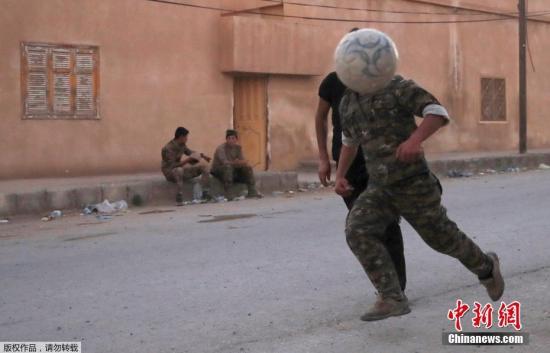 当地时间2017年6月26日，叙利亚拉卡，库尔德战士闲暇时光在街头踢足球。